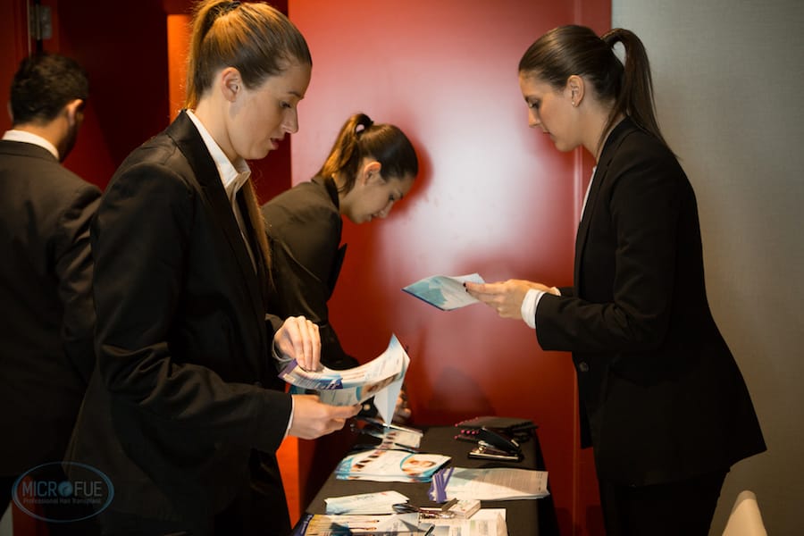 Three young ladies arranging hair transplant pamphlets at a table