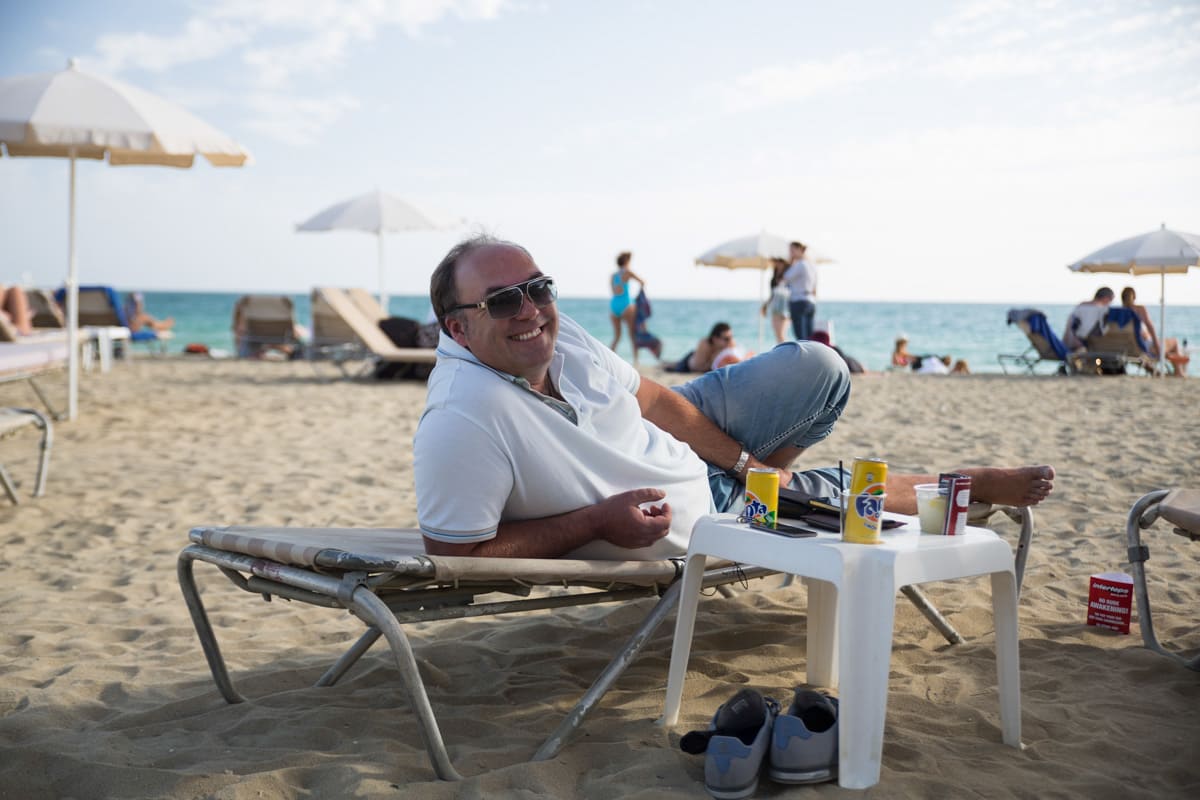 Hombre de negocios sonriente con gafas de sol en la playa acostado en una camilla