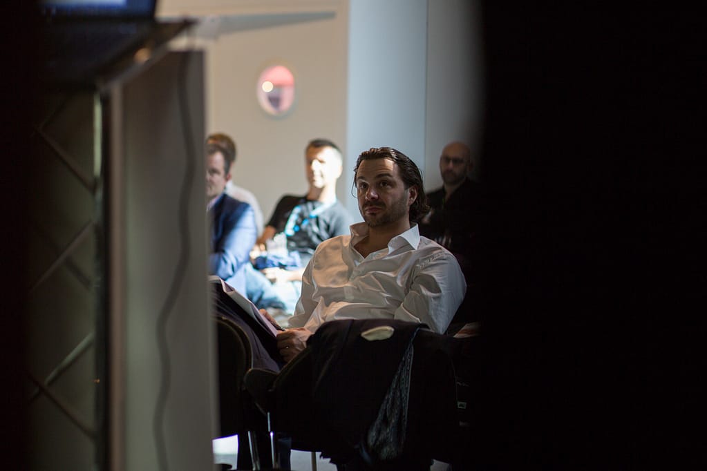 Man in white button down shirt listening to speaker at a business conference, Photo Reportage