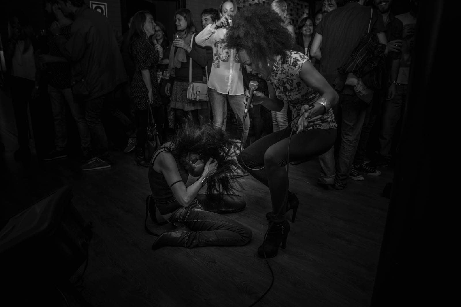 Female singer jumping to the air and another woman kneeling on the ground right next to her